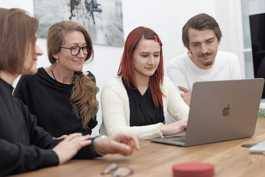 Team chiliSCHARF sitzt gemeinsam vor dem MacBook und plant Marketingstrategien